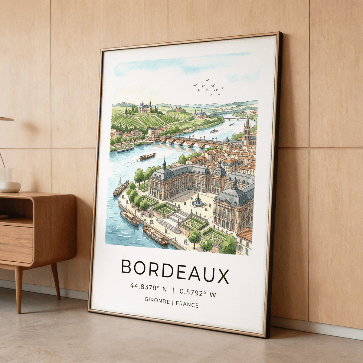 Framed Bordeaux City Art print of a watercolour cityscape leaning against a wooden wall next to a side table