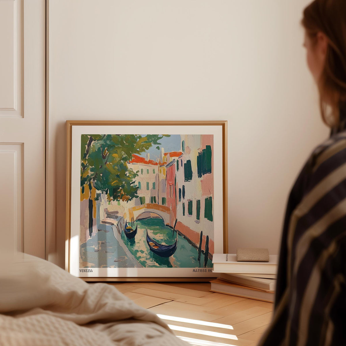 Venice wall art with gondolas in green and pink tones leaning on the floor next to books
