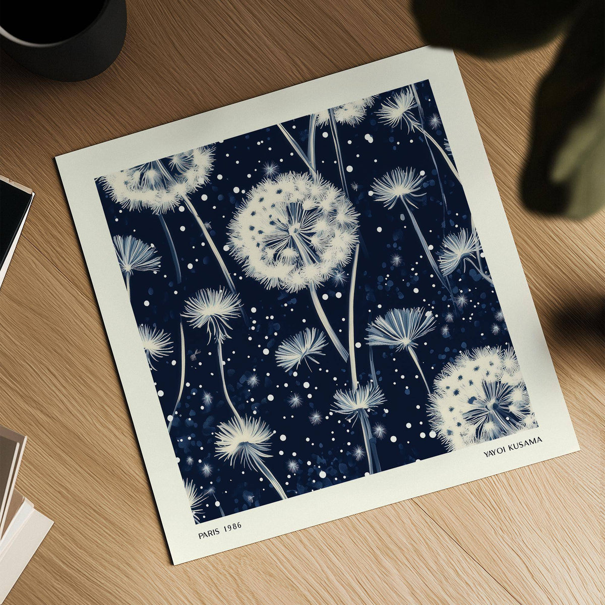 Close-up of navy and white wall art showing dandelion seed heads on a wooden surface with a cup nearby