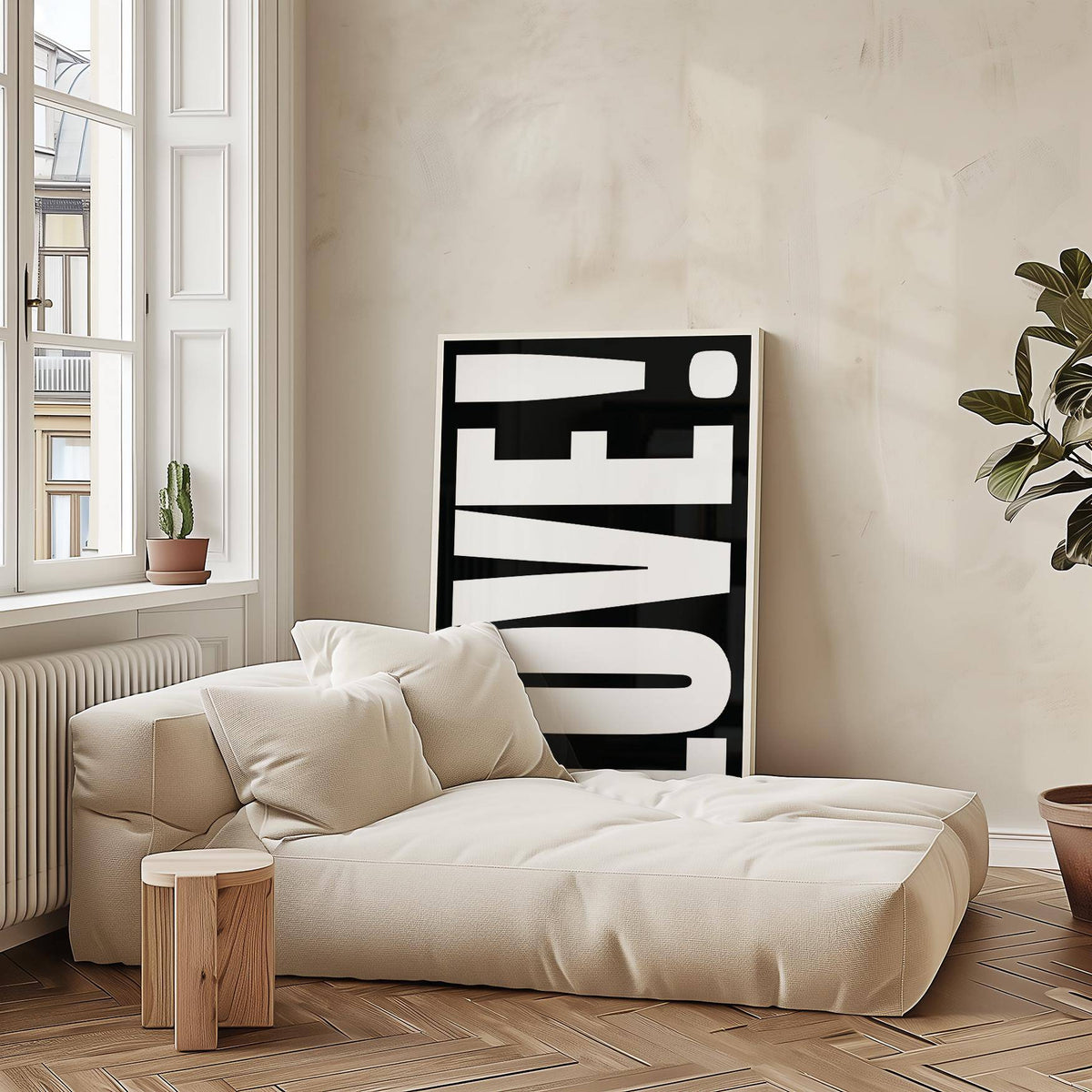 Print leaning on the floor with LOVE typography in black and white beside cream sofa and wooden stool