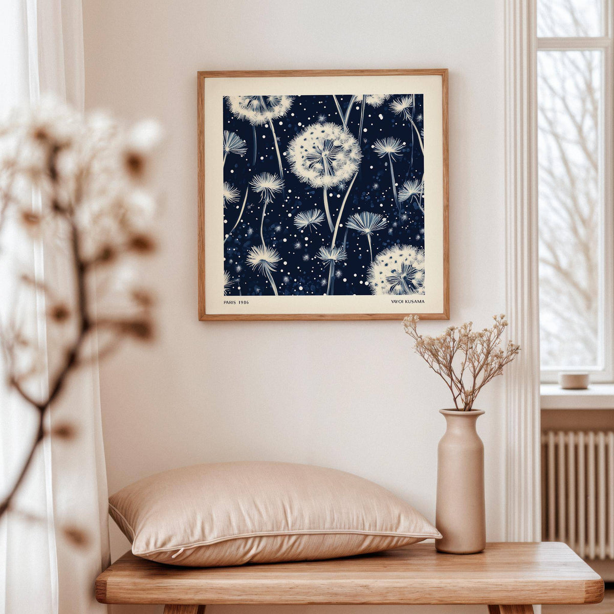 Navy and White wall art of dandelion seed heads hanging on a cream wall above a wooden table with a vase and cushion