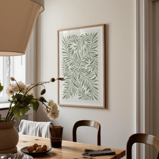Green leaf art print on a cream wall above a wooden dining table with a flower vase