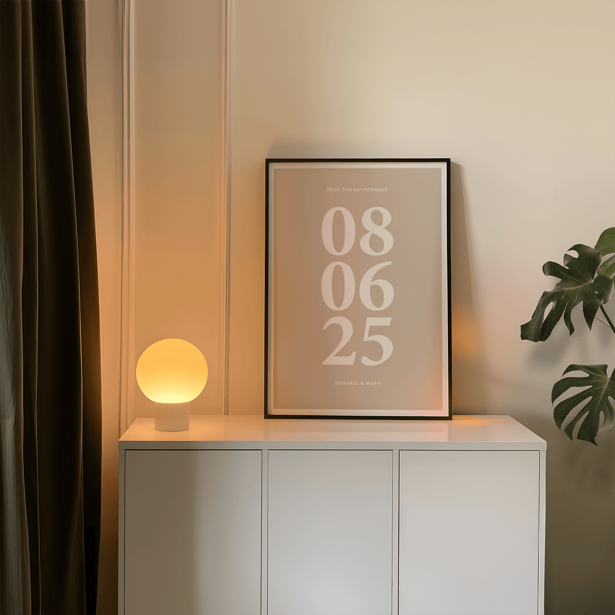 Print leaning on a white cabinet with a glowing lamp and a green plant nearby