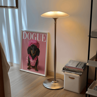 Fashion Dachshund wall art print leaning on the floor near a silver standing lamp and white storage box with magazines