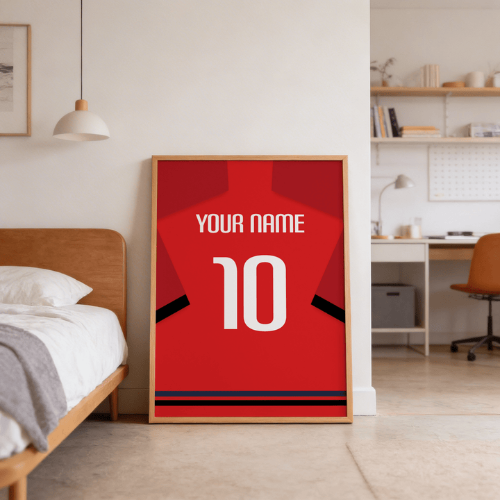 Football Shirt Poster in Red with Black Sleeve Bands leaning against a bedroom wall near a wooden bed