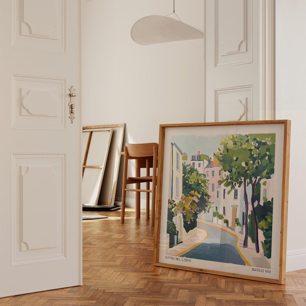 Print leaning on a parquet floor showing a pastel coloured Notting Hill street illustration with trees and buildings