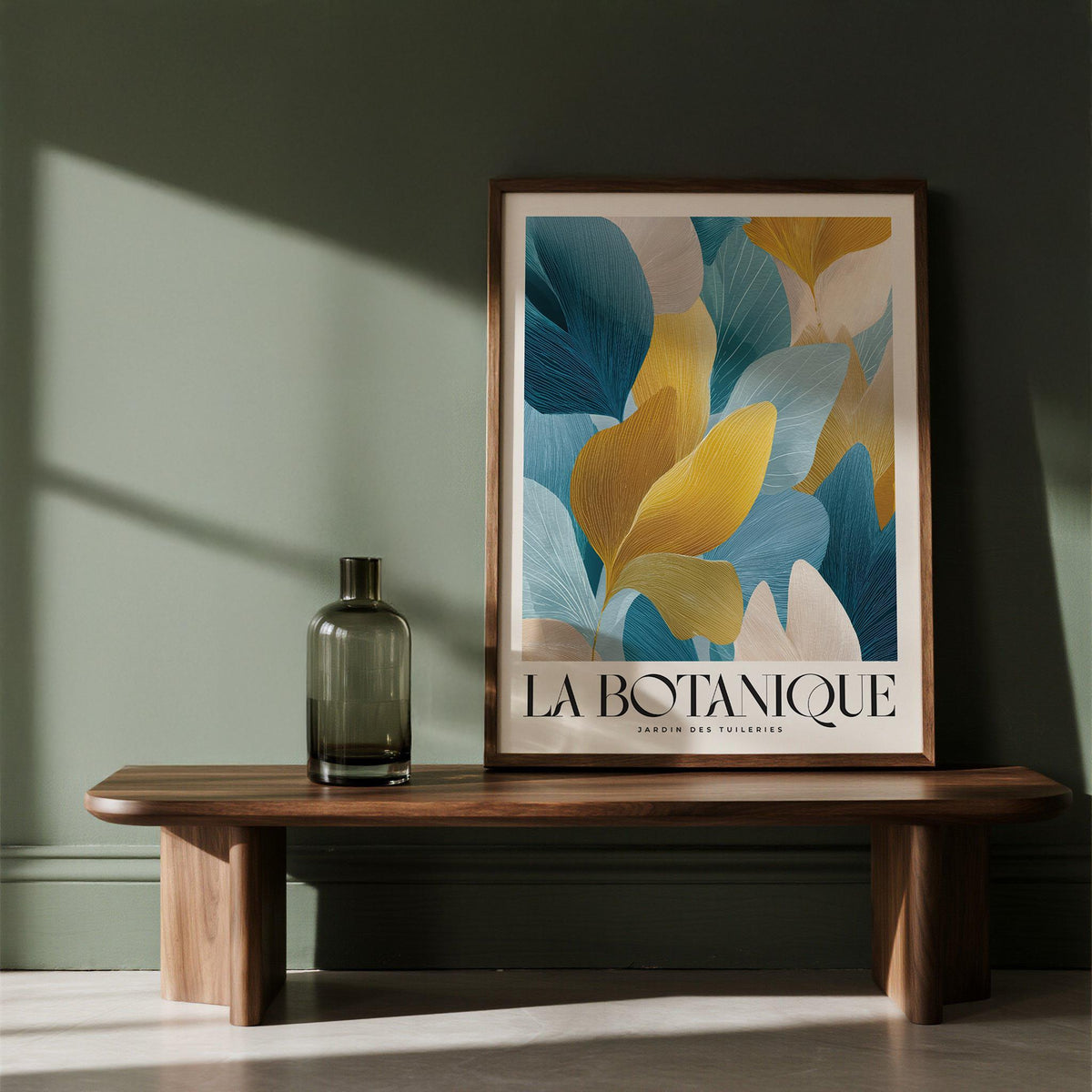 Luxurious wall art of blue and gold leaves framed and leaning on a wooden bench with a green vase nearby