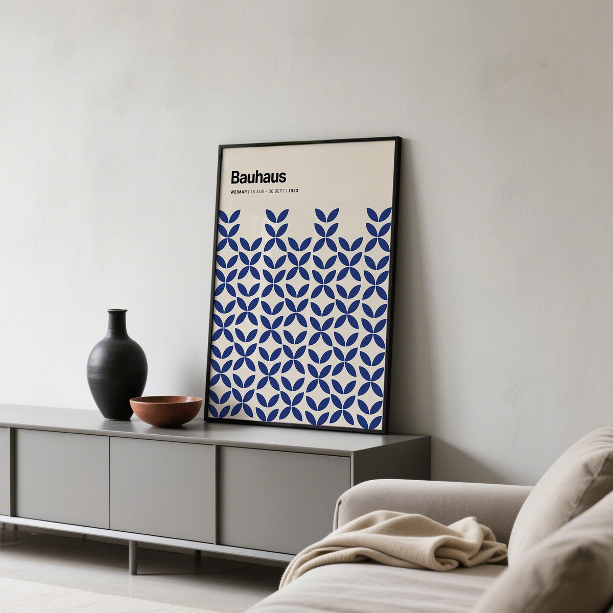 Simple wall art leaning on a grey sideboard with blue geometric pattern and black frame with pottery around