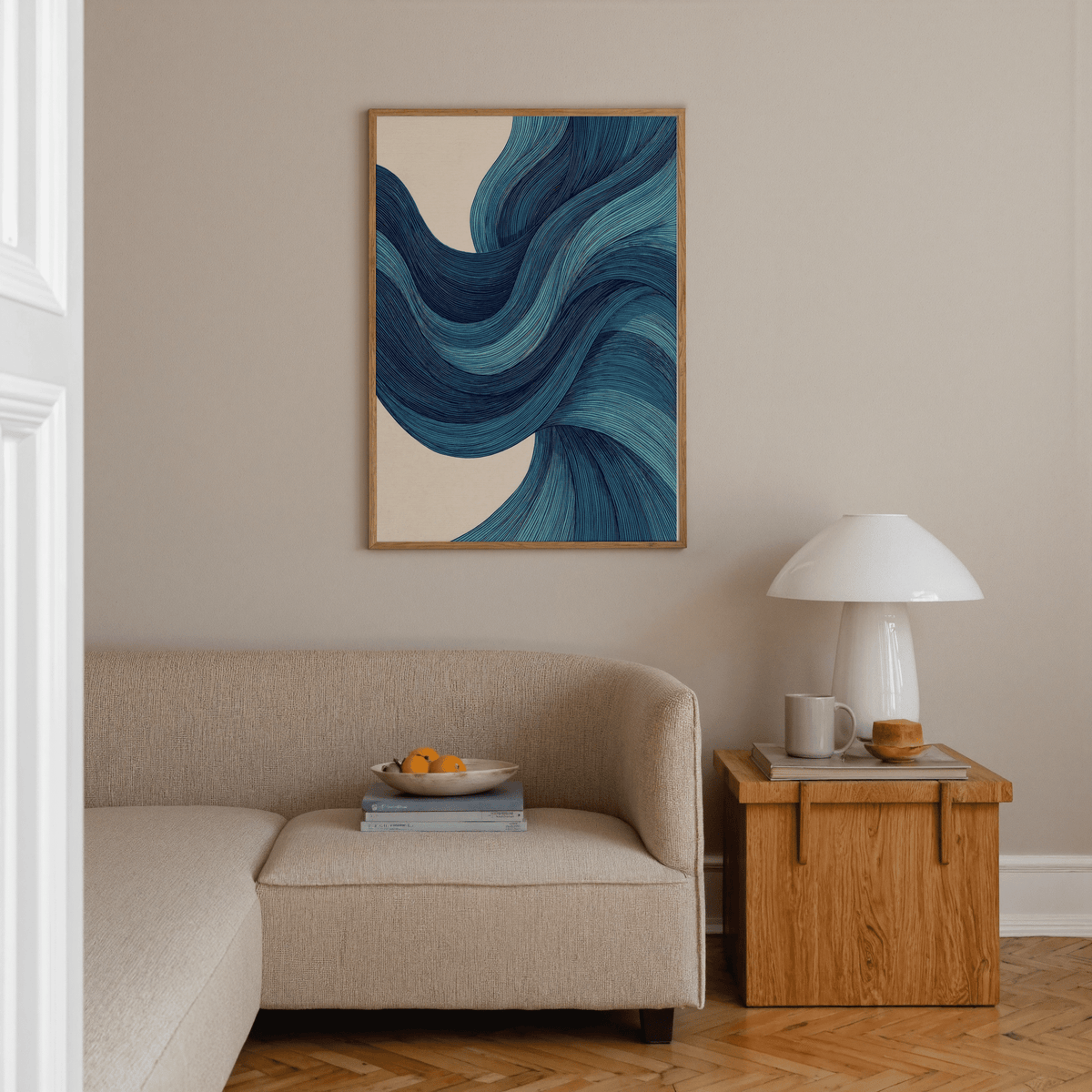 Abstract wave art print with blue wave lines above a beige sofa and wooden side table in a living room