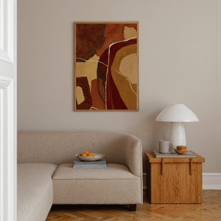 Abstract Earth Tones Print with brown and ochre shapes above a beige sofa and wooden side table in a living room
