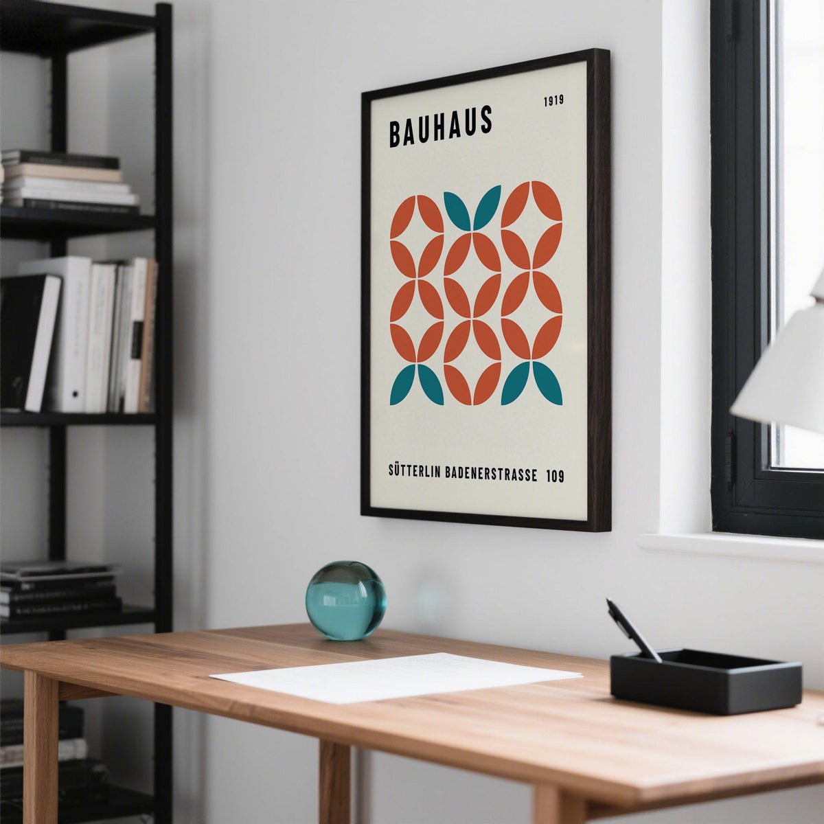 Modern Geometric Wall Art framed print with teal and rust shapes above a wooden desk with a blue glass orb