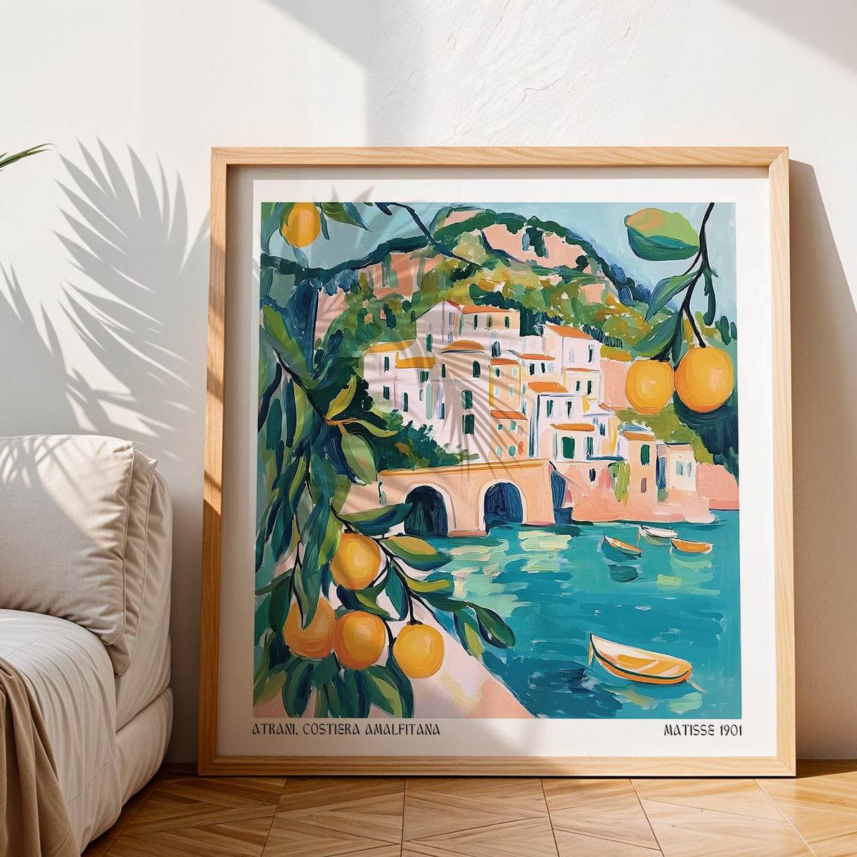 Print leaning on floor of Amalfi Coast Painting showing coastal town with citrus in soft blue and orange tones near a sofa