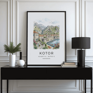 Kotor Landscape Art Print framed with black border showing coastal townscape with mountains and boats alongside a lamp
