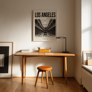 Los Angeles Architecture Art Print on a white wall above a wooden desk with a leather stool and black lamp