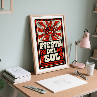 Fiesta Del Sol art print framed with red and cream folk-art design leaning on a desk with sketches and a pink lamp