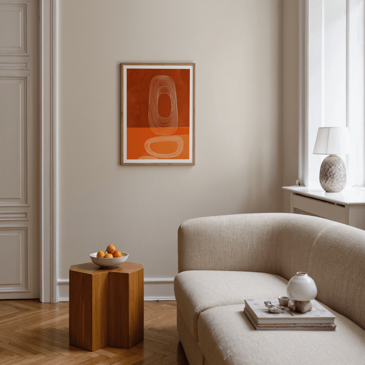 Abstract line art print with nested ovals in rust and orange above a wooden side table