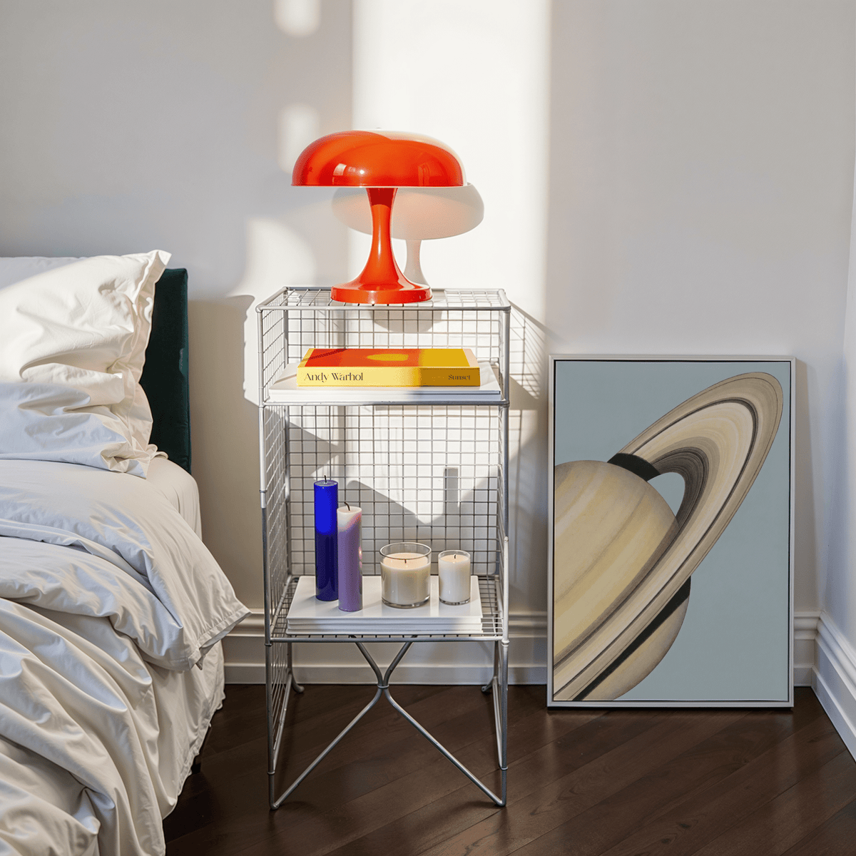 Print of Saturn wall art leaning beside a metal shelf with a red lamp in a sunlit bedroom
