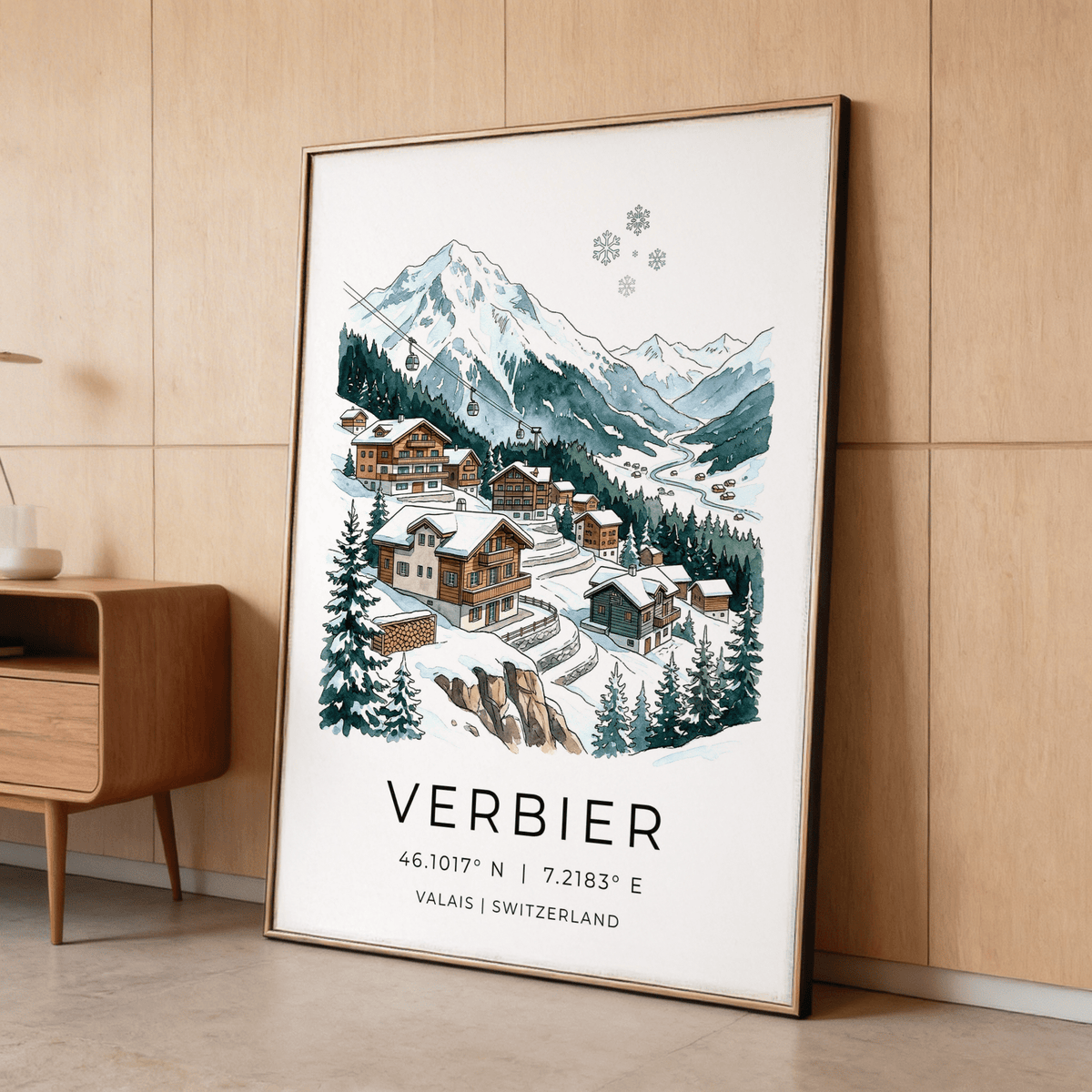 Framed Verbier Mountain wall art of an alpine village with snow and pine trees leaning on a floor against wood panel