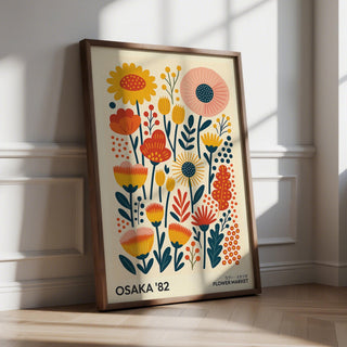Print leaning on floor of stylised flowers in yellow orange and pink with wooden frame