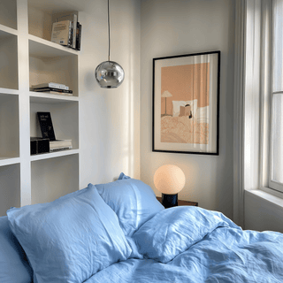 Woman Reading Book Art print of a person reading in bed with beige and white tones hanging above a lamp and blue bedding