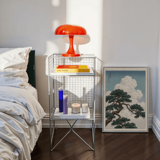 Japanese Landscape Poster print leaning on floor near a bedside table with a red lamp in a bedroom