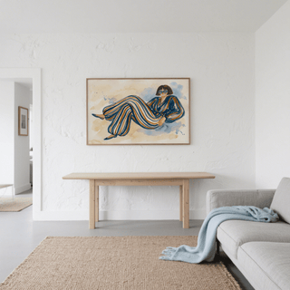 Print on a wall in a living room with a wooden table and grey sofa featuring a woman in a striped jumpsuit