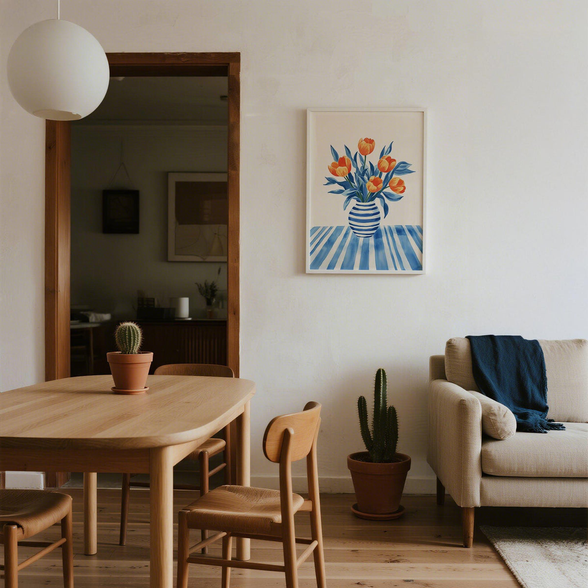 Print on a wall of tulip wall art with orange flowers in a blue striped vase in a dining area with wooden table and cactus