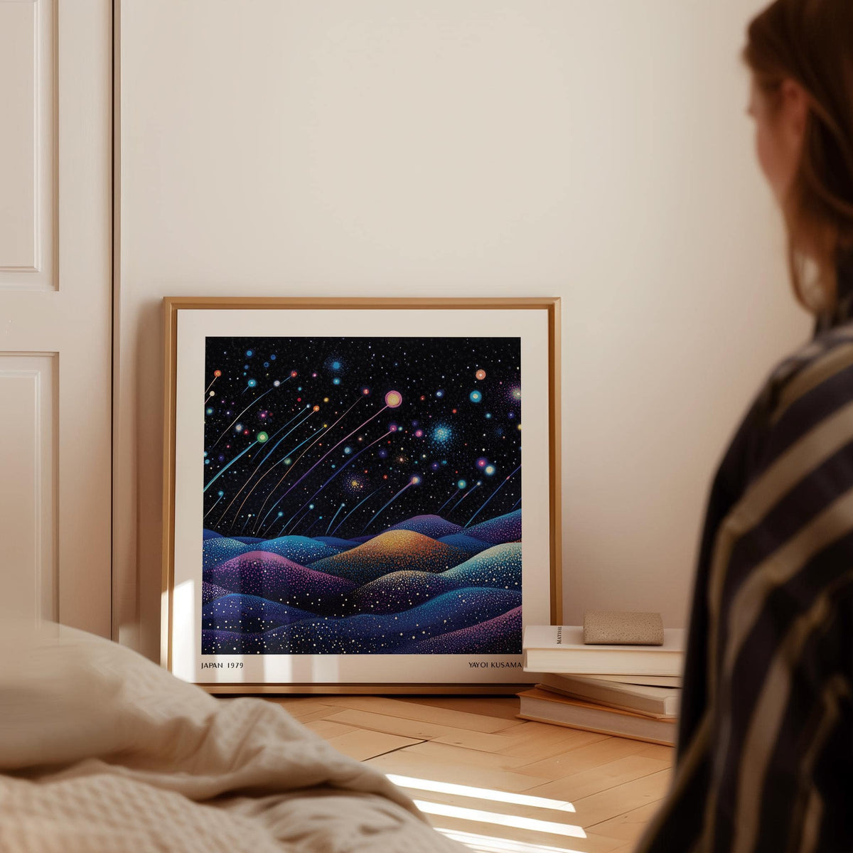 Print leaning on a floor showing shooting stars and colourful hills in abstract style with books nearby