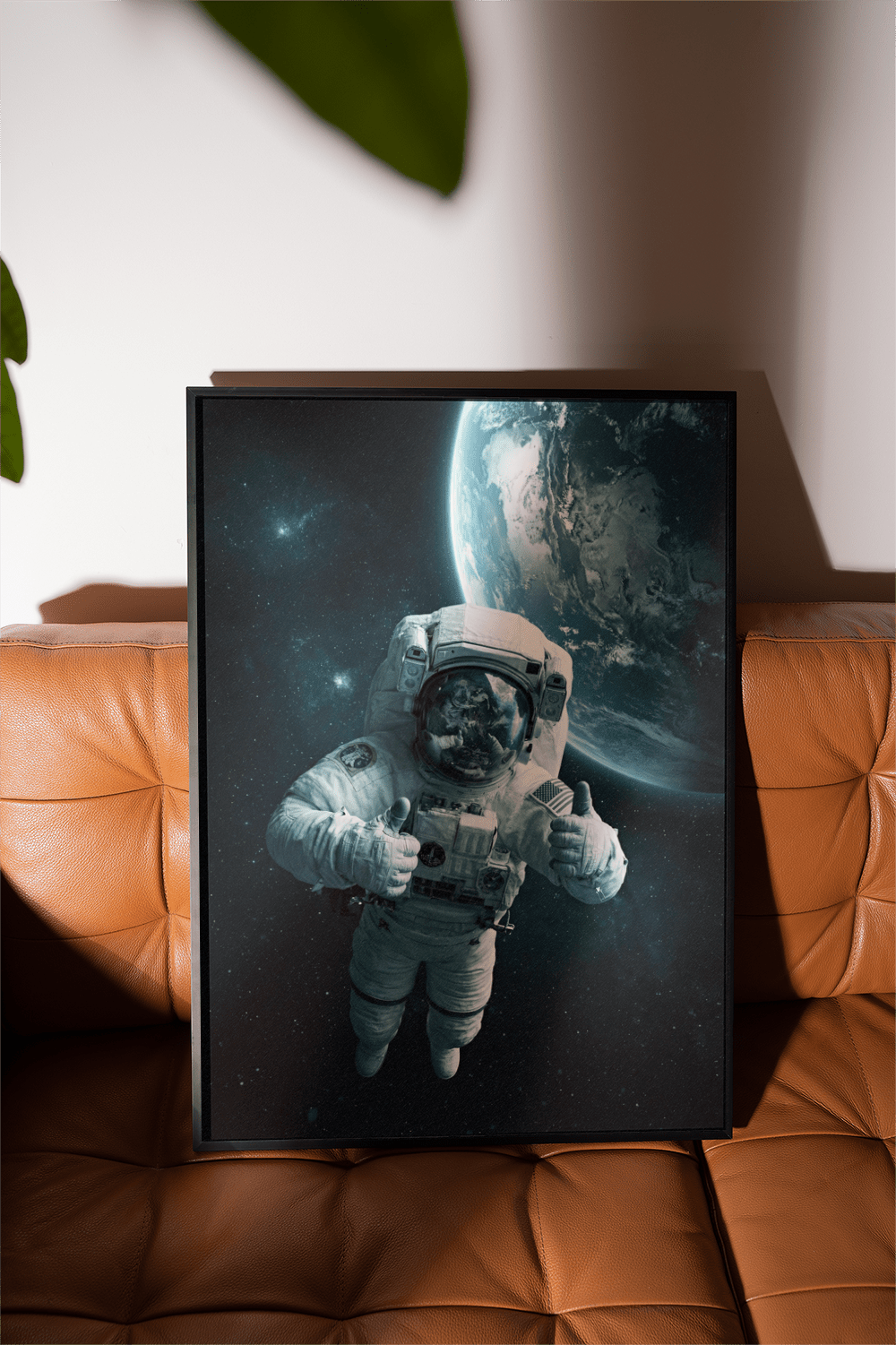 Framed astronaut wall art showing astronaut with planet Earth in the background leaning on a brown leather sofa