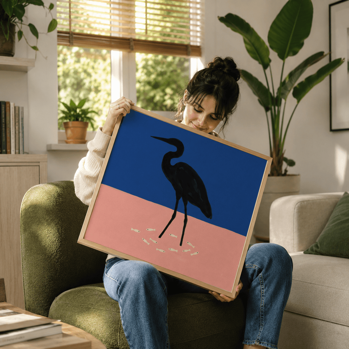 Framed heron art print showing a black silhouette on blue and pink background held by a seated woman