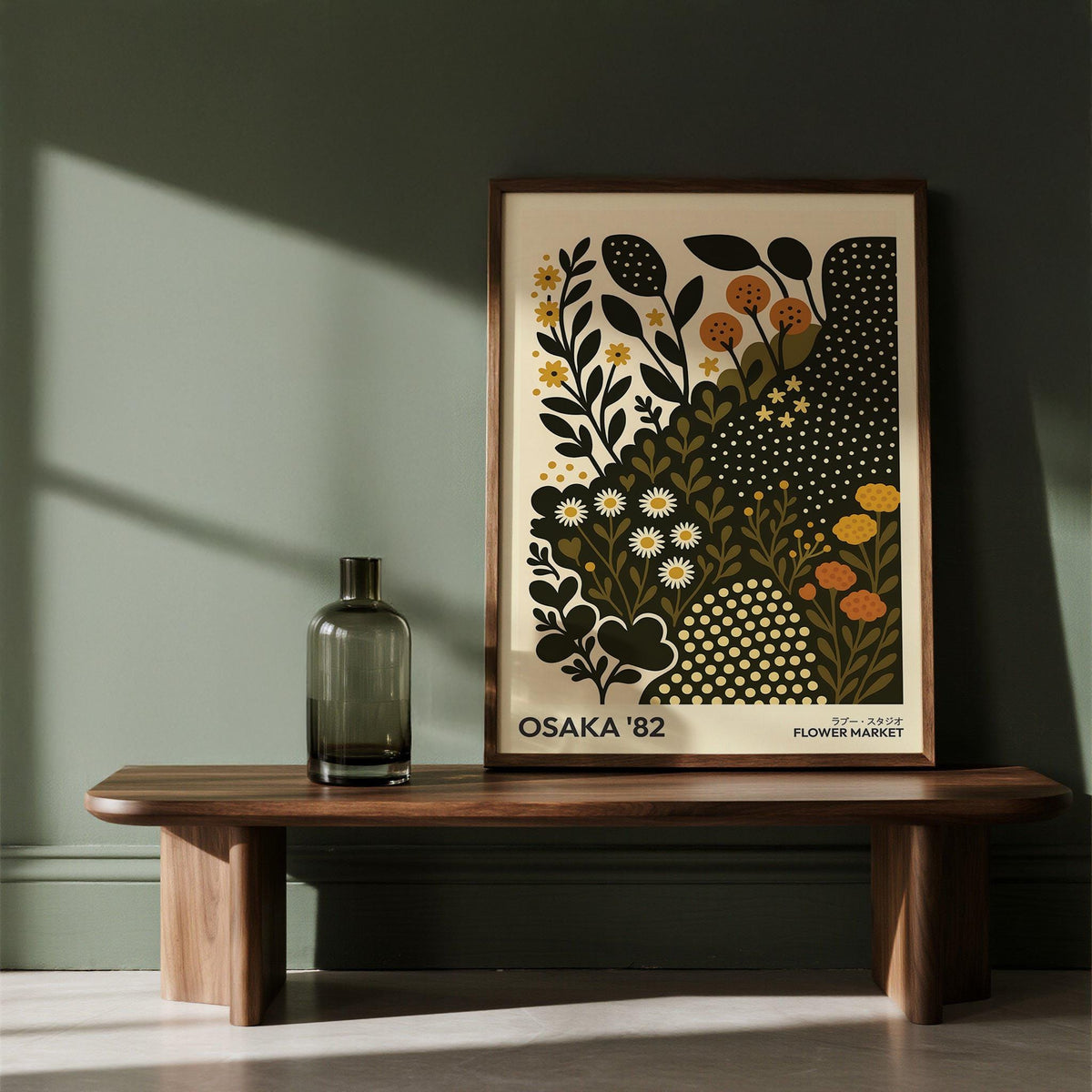Daisy Art Print leaning on a wooden shelf with a green glass vase nearby in a room with dark green walls