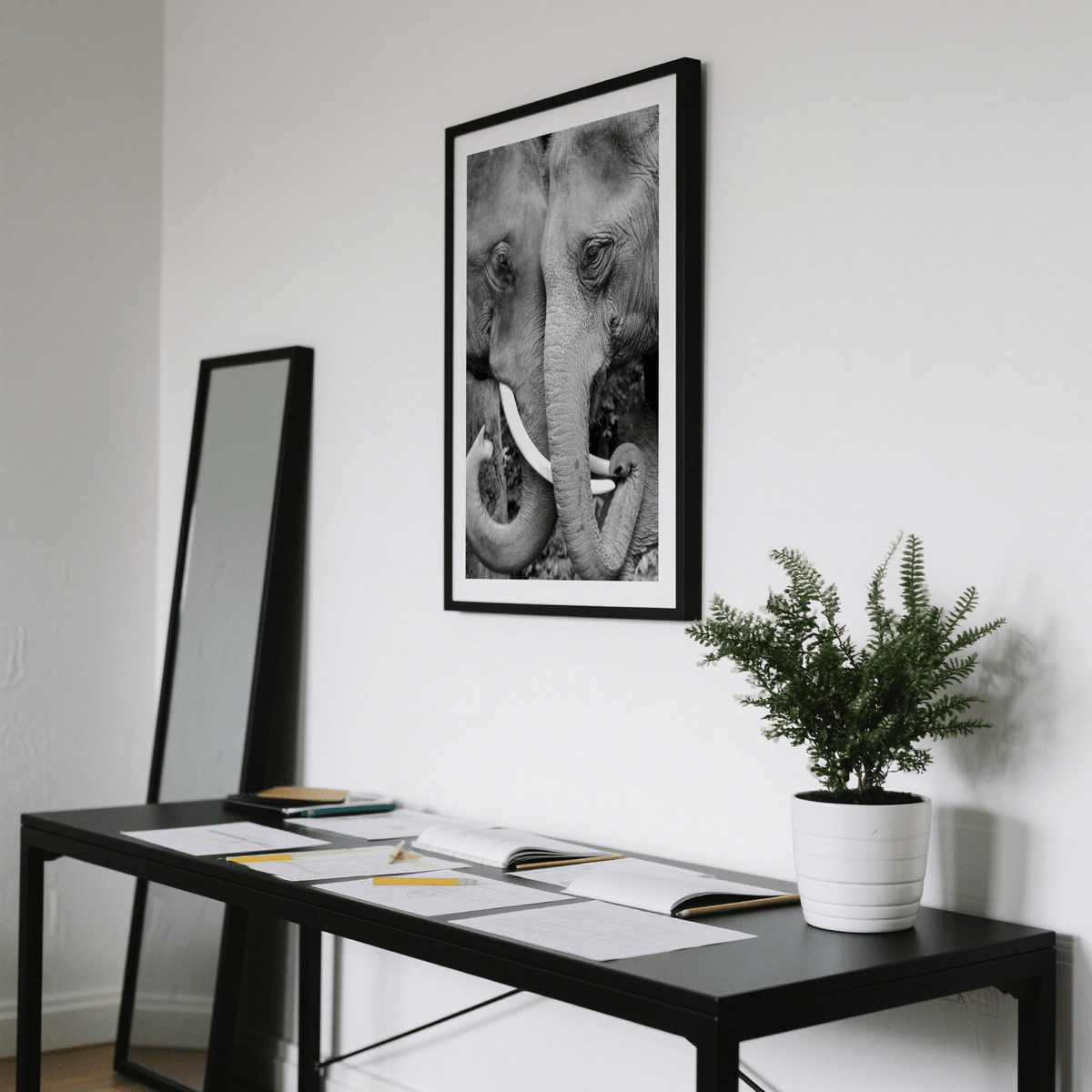 Animal Portrait Art framed print of two elephants touching trunks with black and white tones above a black desk with a white plant pot