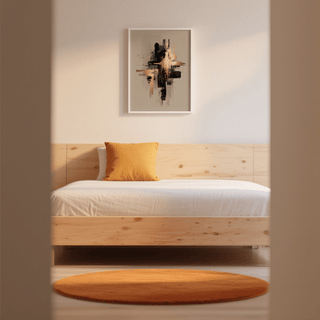 Black and gold poster hung above a wood bed with an orange cushion and round orange rug