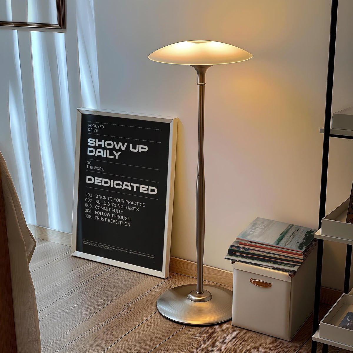 Wall Art Work leaning on wooden floor near a silver lamp and a stack of books
