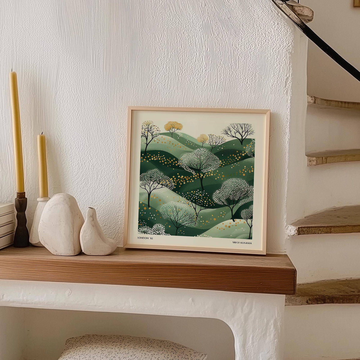 Print leaning on a shelf of stylized green hills with dots and trees with two candles nearby