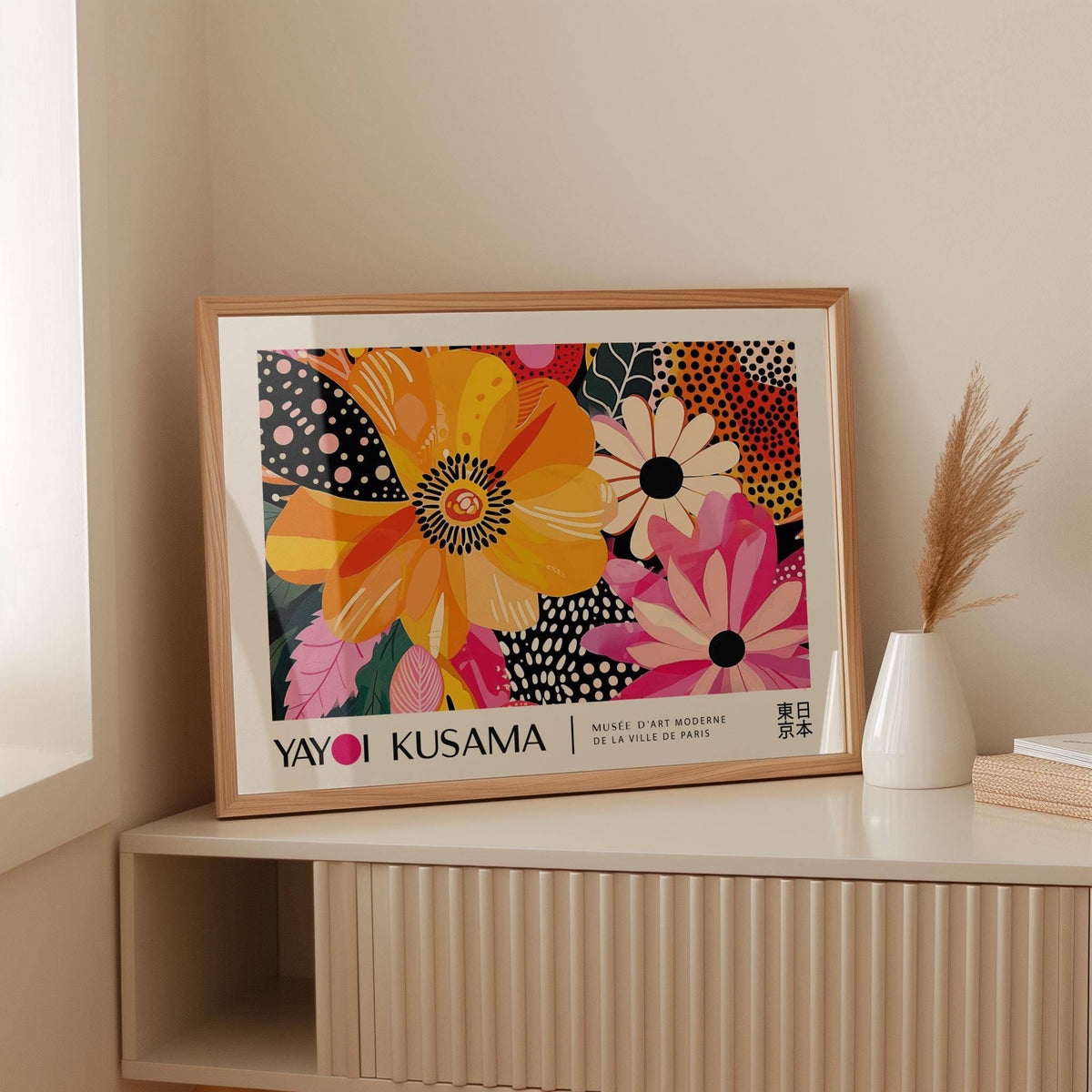 Print leaning on a shelf showing bright abstract flowers in orange pink and black with a white vase nearby