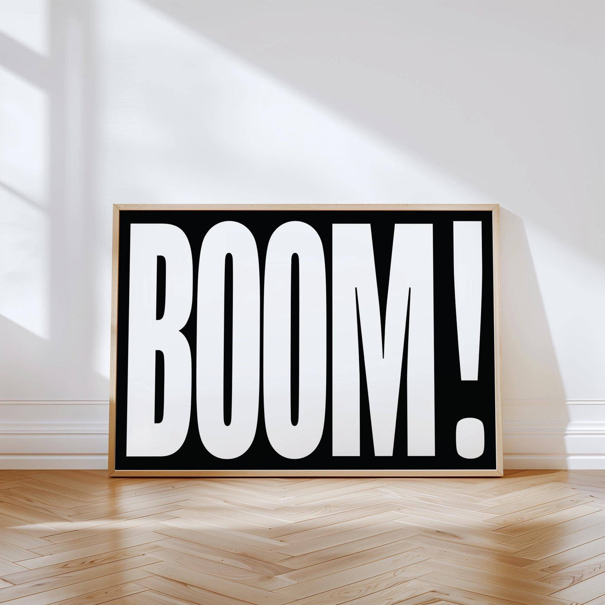 Print of modern typography wall art with white BOOM text on black leaning against a wall on a wooden floor