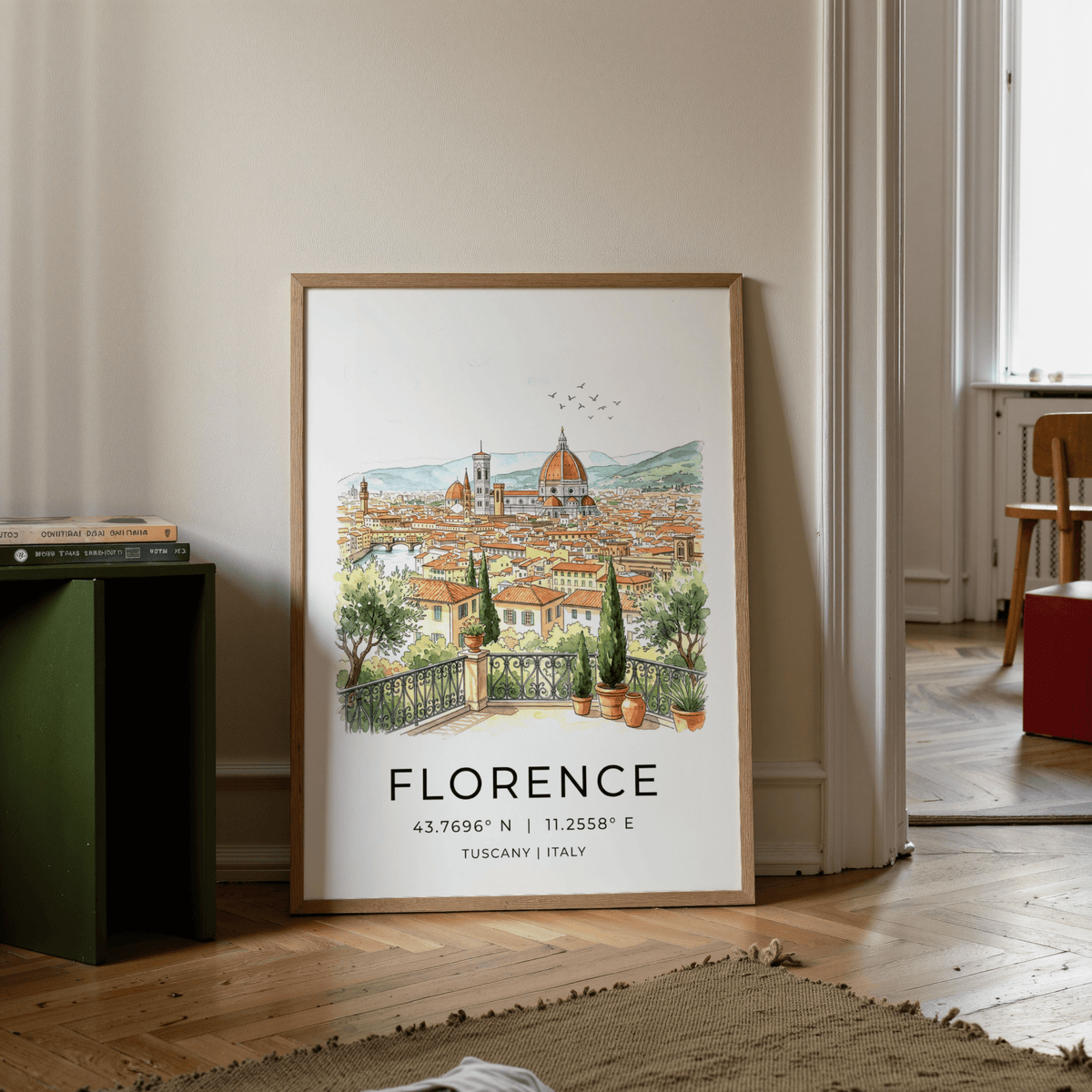 Florence Italy art print leaning on floor showing a watercolour cityscape with orange roofs and green plants beside a stack of books
