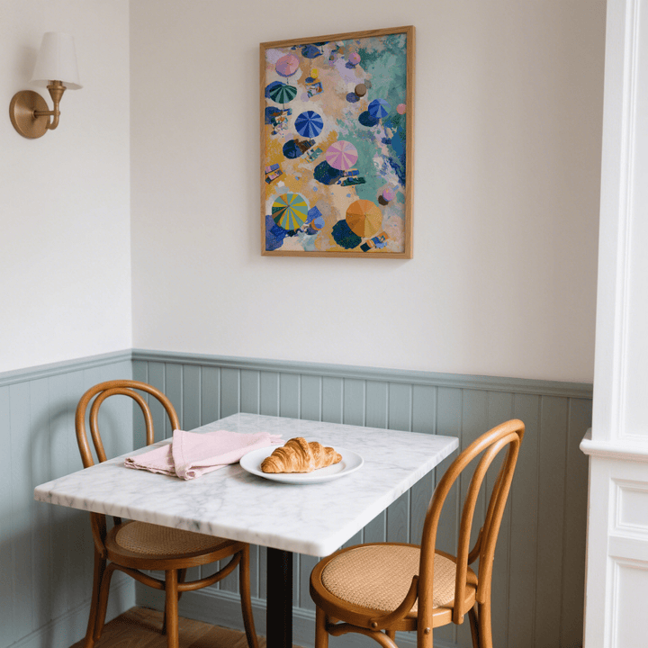 Beach Umbrellas Print above a small dining table with croissant and wooden chairs in a muted blue corner