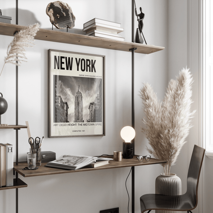 Empire State Building wall art in black and white with bold text above a desk with a lamp and pampas grass