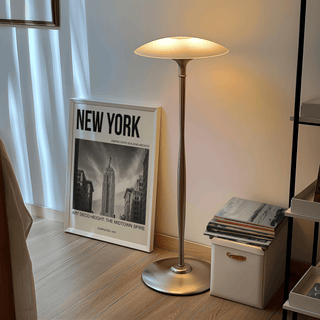 Empire State Building wall art leaning on wooden floor next to a tall lamp and a stack of books