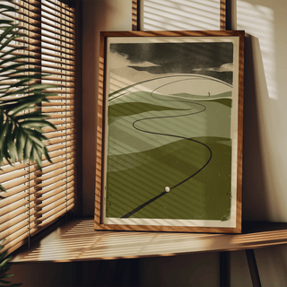 Print leaning on a shelf showing a minimalist retro golf ball on winding fairway with green and beige colours and a plant nearby