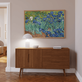Blue Iris wall art with blue flowers in a light wooden frame above a sideboard with a white lamp