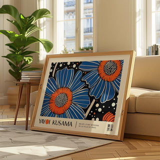 Print leaning on a floor with blue flower art in pop-art style beside a beige sofa and plant