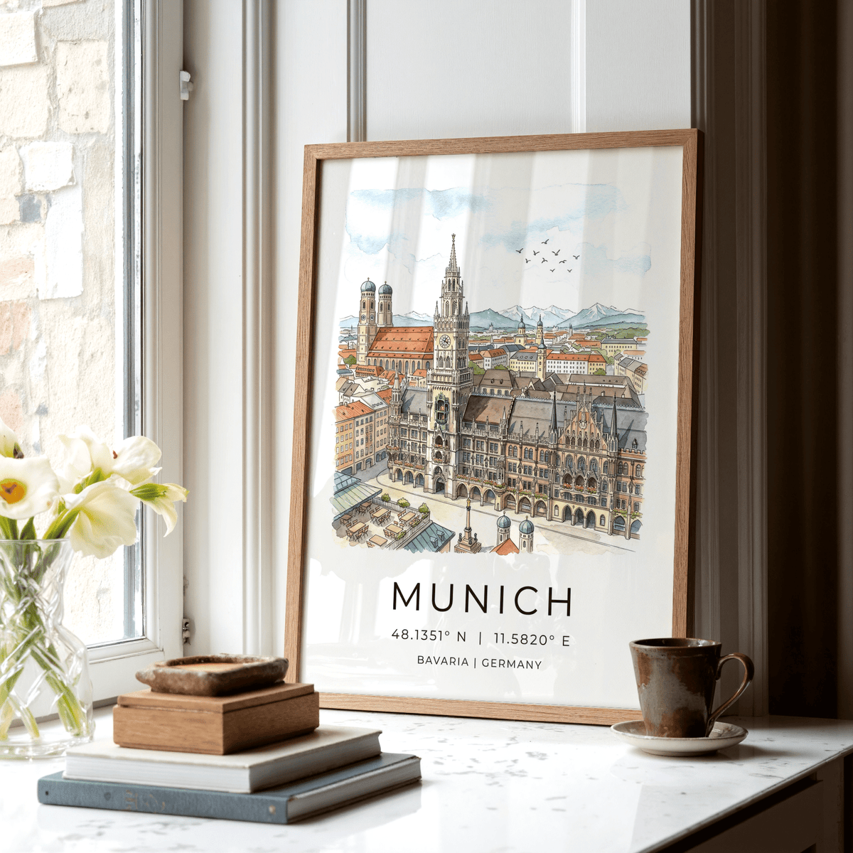 Print leaning on a shelf of Munich city wall art illustration in soft watercolour tones with books and cup nearby