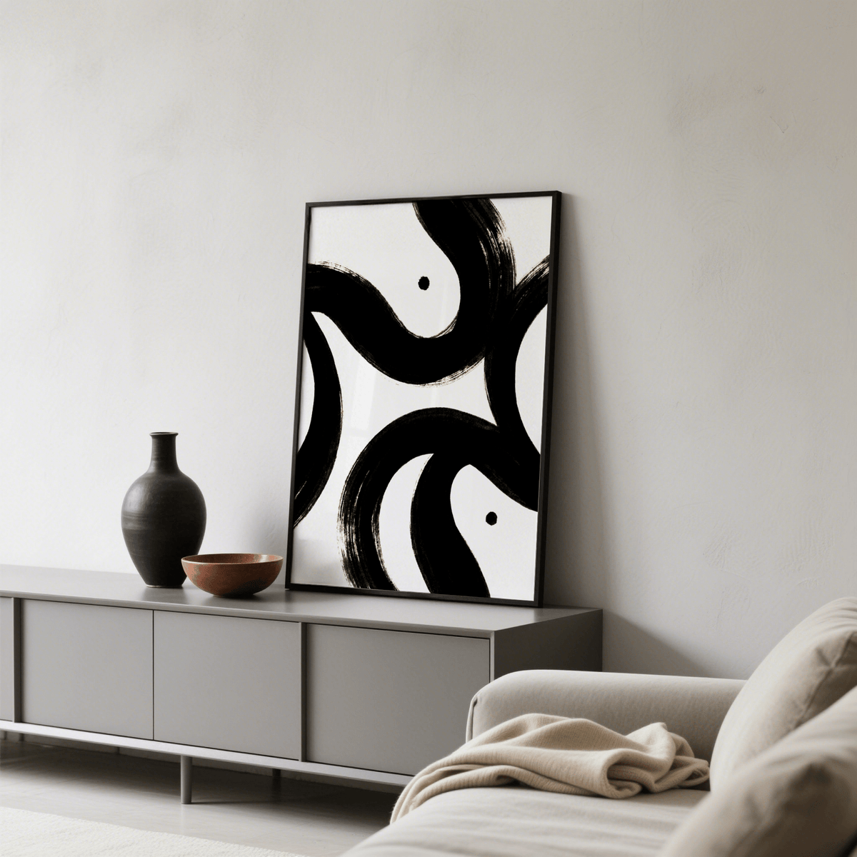 Black and White Posters leaning print with bold black abstract brush strokes near a black vase on a grey sideboard