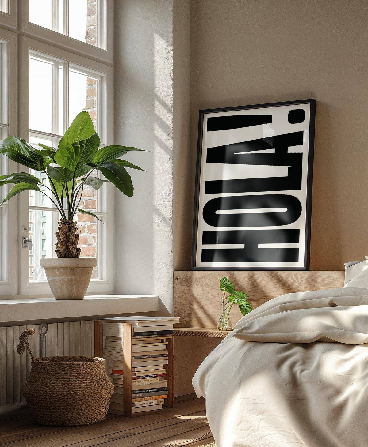 Framed print leaning showing bold black HOLA typography next to a leafy houseplant in a bedroom