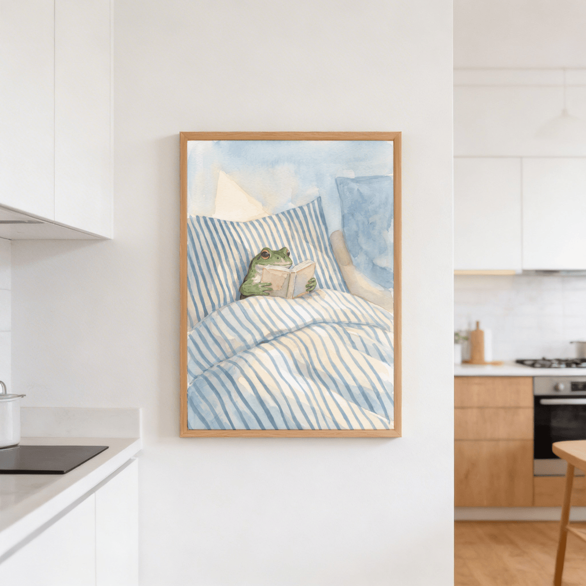 Print of frog reading in bed with blue and white stripes hanging in a kitchen