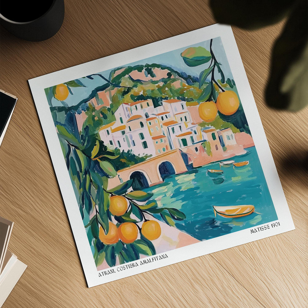 Amalfi Coast painting showing a coastal town with citrus on a wooden table with books nearby