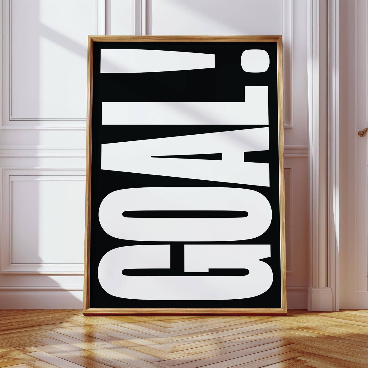 Print leaning on the floor with large white GOAL typography on a black background in a bright room